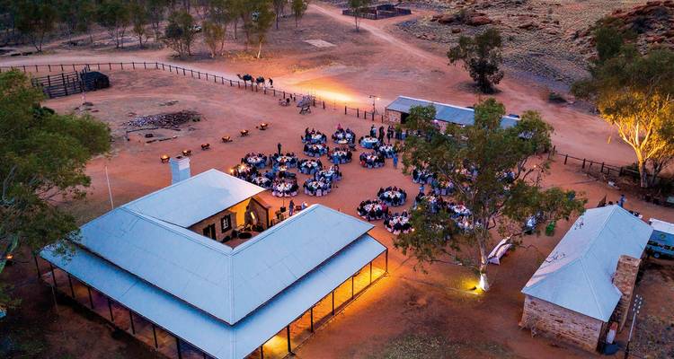 Vue aérienne d'un rassemblement en plein air dans un lieu rural avec des tables installées autour d'un bâtiment central.