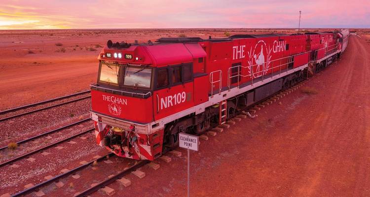 Le train Ghan dans un paysage désertique avec un ciel de coucher de soleil coloré.