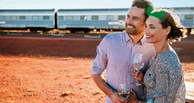 Couple debout près d'un train tenant des verres de vin.