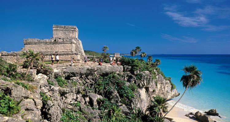 Ancient Tulum cliff-top ruins overlooking turquoise Caribbean waters and white beach below.