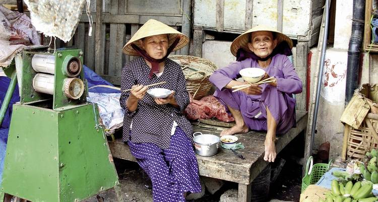 Zwei Frauen in traditioneller Kleidung essen im Freien.