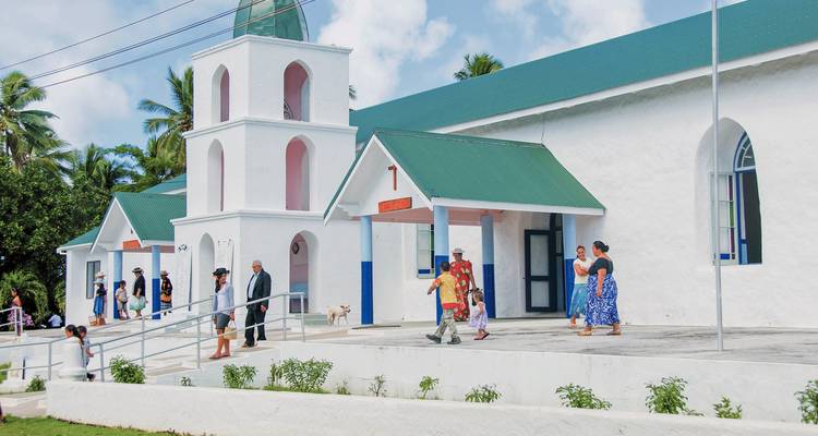 Wit kerkgebouw met mensen verzameld buiten.
