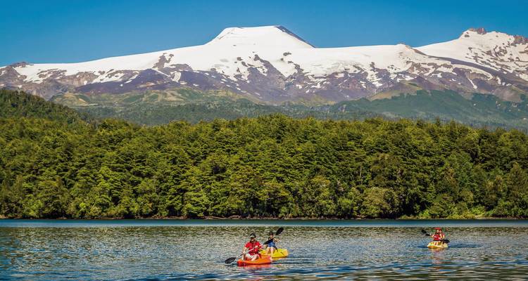 Kayakers on a lake with a snow-capped mountain in the background.
