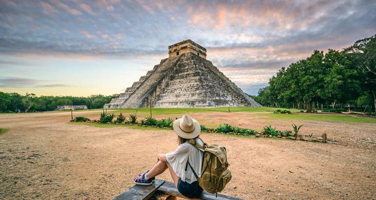 Vrouw zittend voor een iconische Maya-piramide tijdens zonsondergang.