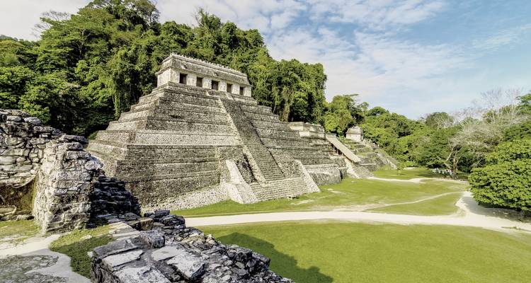 Grote oude piramide omringd door bos en heldere hemel.