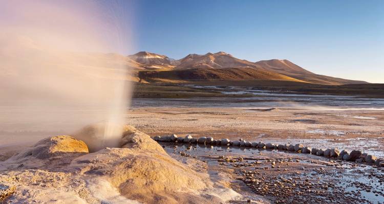 Geysir, der in einer bergigen Landschaft unter blauem Himmel ausbricht.