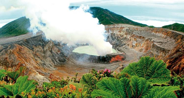 Volcano with smoke and surrounding lush hills.