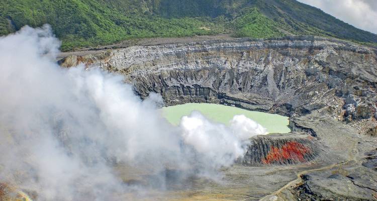 Volcanic crater with smoke plume and rugged terrain.