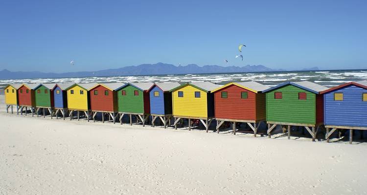 Strand mit bunten Strandhütten und Bergen im Hintergrund.