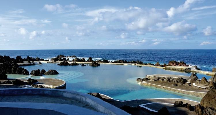 Piscine océanique avec paysage rocheux et nuages.