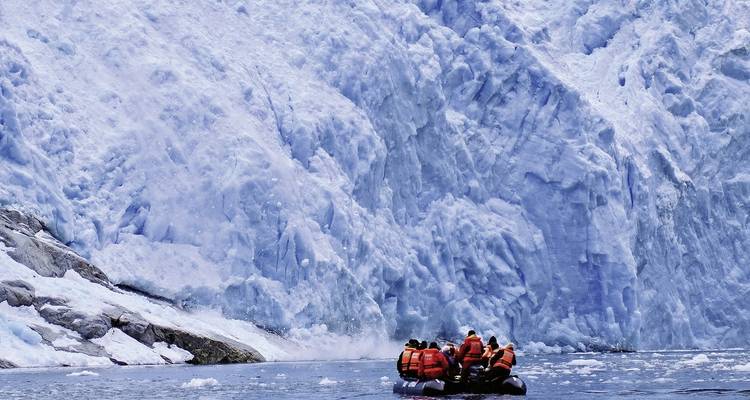 Bateau avec des personnes s'approchant d'une grande façade de glacier.