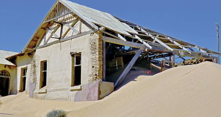 Abandoned house partially buried in sand dunes.