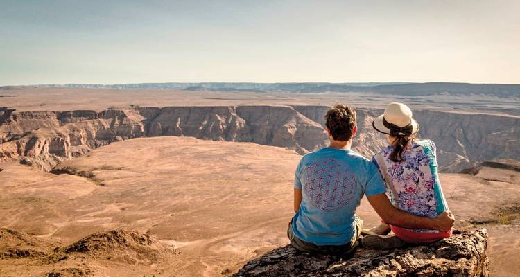 Pareja sentada en un acantilado con vista a un vasto cañón.