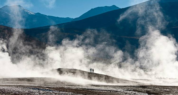 Geisers met nevel en verre figuren in een vulkanisch landschap.