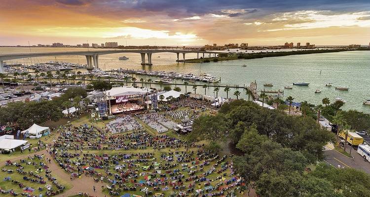 Crowd gathered for an event by the waterfront with a bridge in the background.