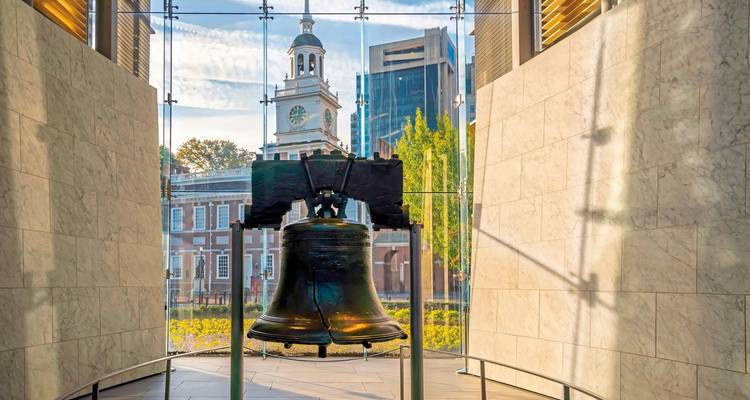 La Campana de la Libertad dentro de un pabellón con edificios históricos afuera.