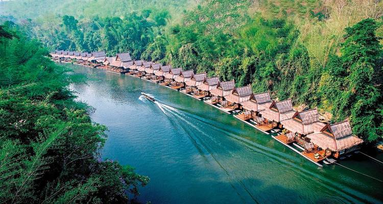Aerial view of a river lined with floating houses, surrounded by lush greenery, with a boat moving through the water.
