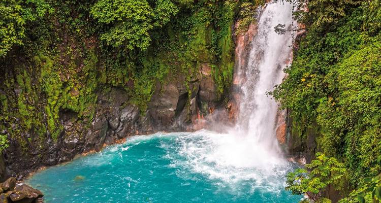 Wasserfall, der in ein blaues Becken stürzt, umgeben von üppigem Wald.