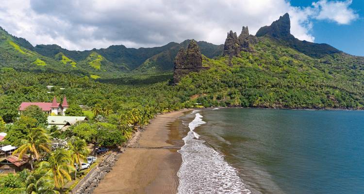 Montagnes verdoyantes luxuriantes et plage de sable bordée de palmiers.