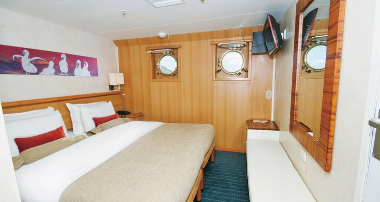 Innenraum einer kleinen Kabine mit zwei Einzelbetten und Bullaugen.