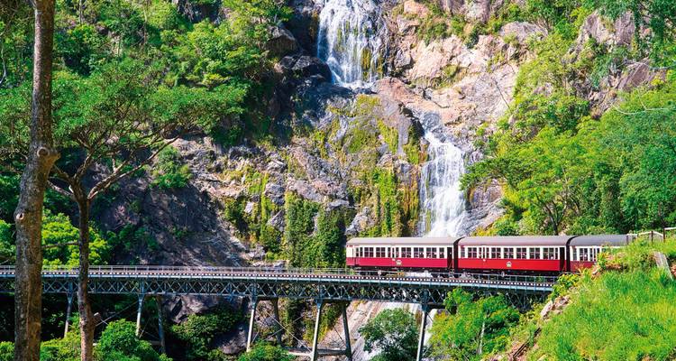 Eine malerische Zugfahrt über eine Brücke mit einem Wasserfall im Hintergrund.