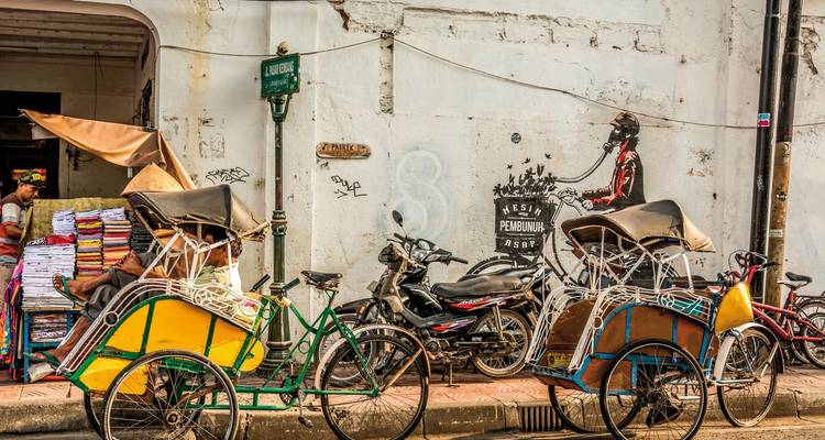 Scène de rue avec des pousse-pousse et des motos garés le long d'un mur.