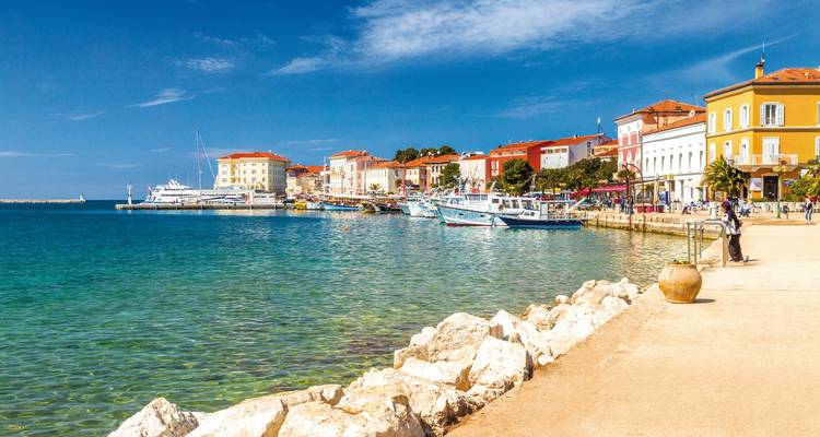 Eine Küstenstadt mit hellen Gebäuden entlang einer türkisfarbenen Uferpromenade.