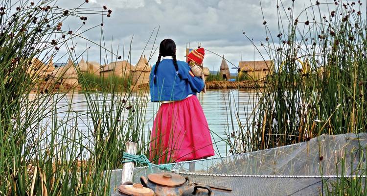 Frau in traditioneller Kleidung steht an einem See mit strohgedeckten Gebäuden.