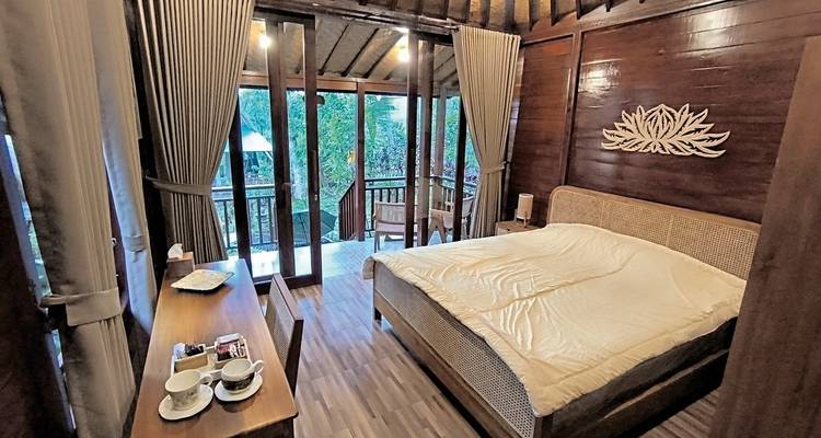 Intérieur d'une chambre en bois chaleureuse avec un grand lit et des fenêtres donnant sur la verdure.