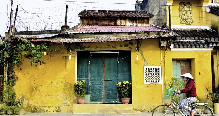 Altes Gebäude mit rustikaler Fassade, Frau fährt Fahrrad davor.