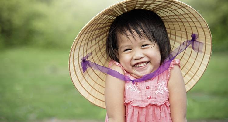 Junges Mädchen, das breit lächelt, während es einen traditionellen Hut trägt.