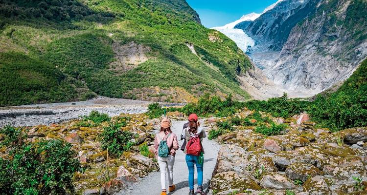Deux personnes marchant vers un glacier à travers une vallée luxuriante.