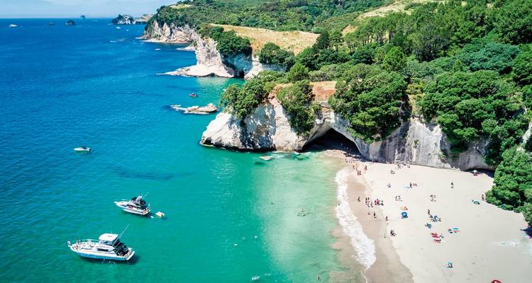 Une belle plage avec des gens, des bateaux, de l'eau claire et des falaises.