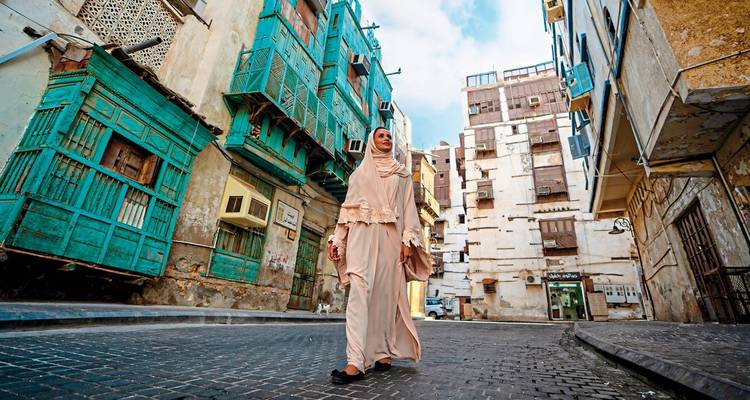 A woman walking through an old city with traditional wooden windows.
