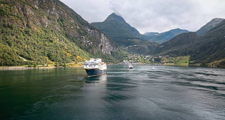 Cruise ship sailing in a fjord surrounded by steep mountains.