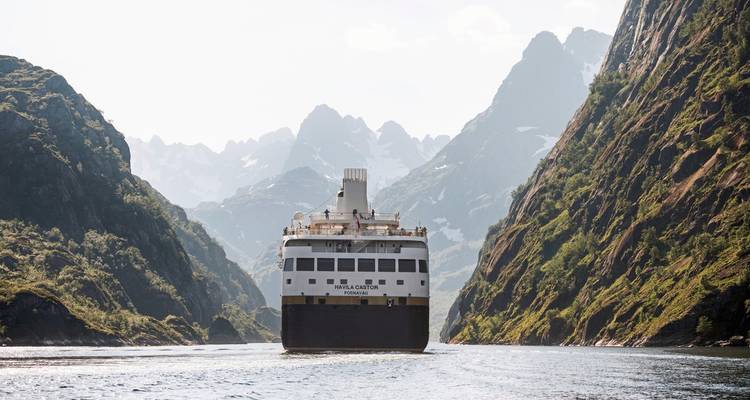 Cruise ship navigating in a narrow mountainous fjord.