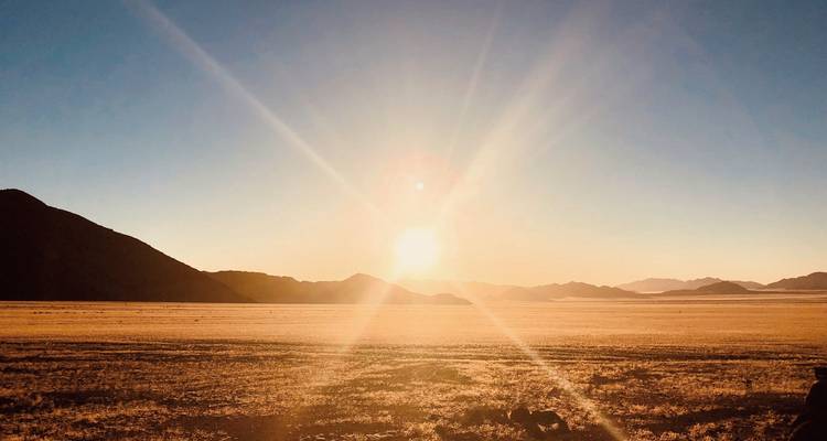Open desert landscape with setting sun and mountains.