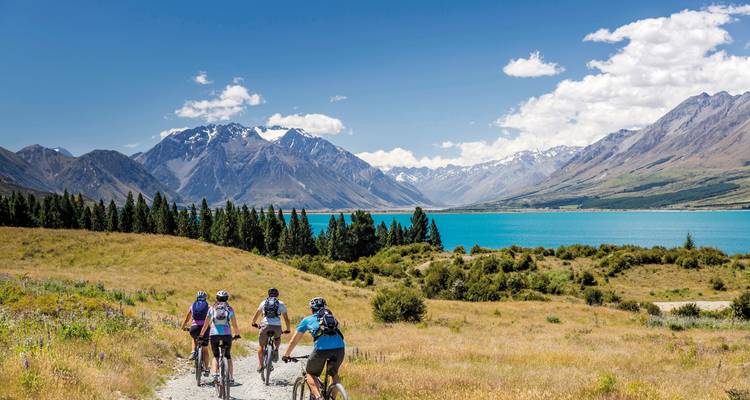 Cyclists riding along a scenic lake with mountains.