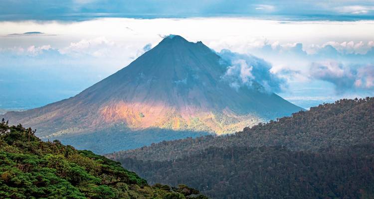 Volcan majestueux entouré de forêt et de couverture nuageuse.