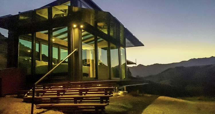 Cabane moderne en verre avec éclairage du soir dans une région montagneuse.