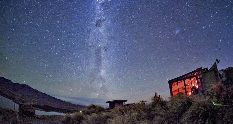 Ciel nocturne étoilé avec un chalet moderne et la Voie lactée visible.