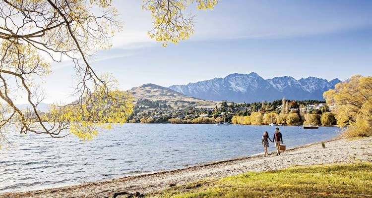 Un couple se promenant le long d'un lac avec une ville et des montagnes en arrière-plan.