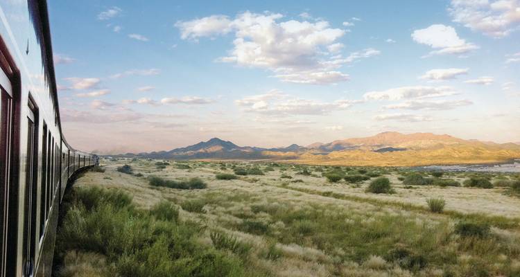 Zug, der durch eine malerische Landschaft mit Bergen im Blick fährt.