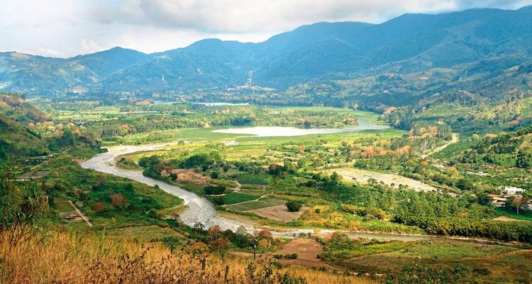 Vallée verdoyante luxuriante avec une rivière sinueuse et des montagnes au loin.