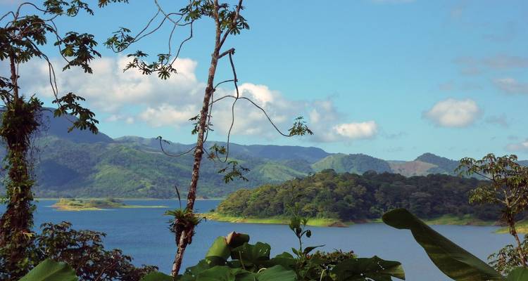 Landschaft mit einem See, umgeben von üppig grünen Bergen und einem klaren blauen Himmel.