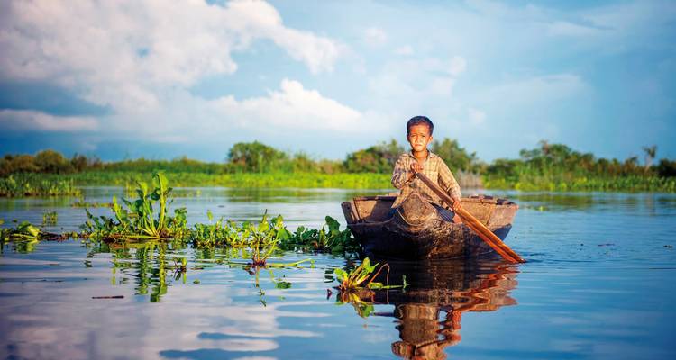 Ein Kind, das ein Boot auf einem ruhigen Gewässer mit üppigem Grün rudert.
