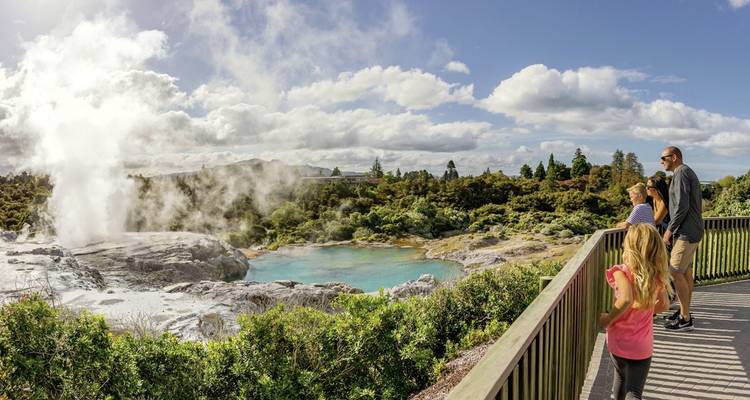 Familie beobachtet einen geothermalen Geysir mit aufsteigendem Dampf.