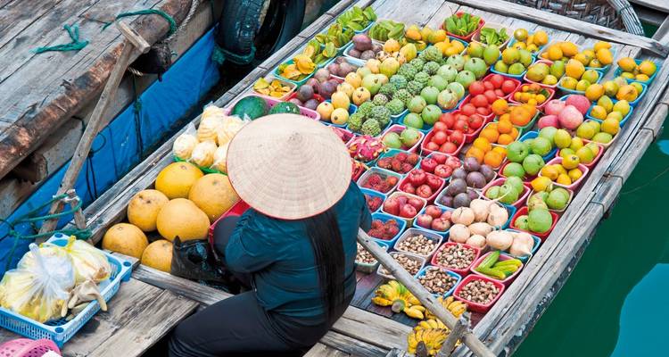 Personne sur un bateau rempli de fruits et légumes colorés dans un marché flottant.