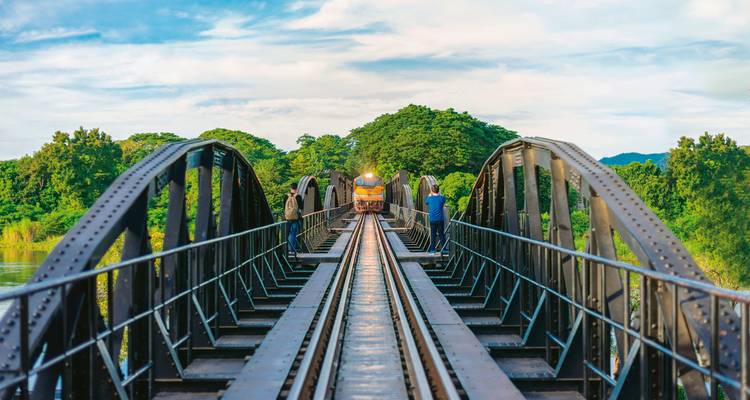 Train traversant un pont historique entouré d'une végétation luxuriante et de montagnes.