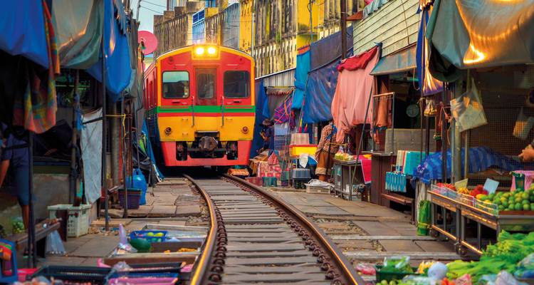 Zug fährt durch einen belebten Markt mit Ständen nahe den Gleisen.